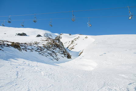 A ski lift ascends a mountain at the San Isidro-Zona Cebolledo ski resort in Spain. Winter sports enthusiasts enjoy the snowy slopes and a cozy chalet nestles nearby.