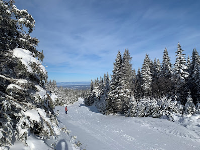 A skier enjoying a day at Massif du Sud ski resort in Quebec with a ski lift in the backdrop amidst scenic winter surroundings.
