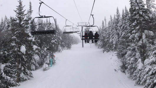 A ski lift ascends a snow-covered slope at Massif du Sud ski resort in Quebec Canada. Skiers are enjoying winter sports amidst the beautiful snowy landscape.