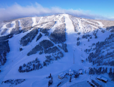 A ski resort in Neihart Montana featuring a ski lift and snow-covered slopes with skiers enjoying winter sports.