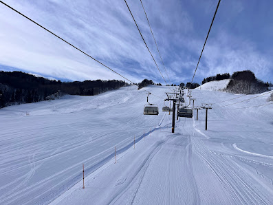 Ski resort scene at Chokai Kogen Yashima in Akita, Japan. Features a ski lift leading up to a challet amongst pristine white snow, with individuals engaging in various winter sports activities.