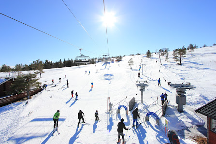 Skiers enjoying a sunny day at the Vrådal Panorama resort in Norway. The image shows snowy slopes, ski lifts and a bustling ambience of a winter sports centre.