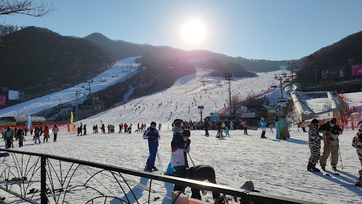 Winter scene at Konjiam Resort, South Korea featuring skiers enjoying the snow covered slopes, a chalet tucked amidst the stunning winter landscape, and signs of a bustling winter sports centre.