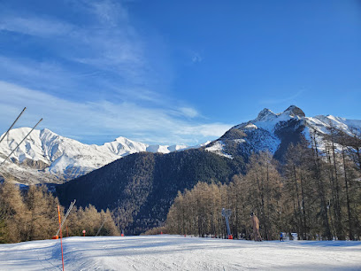 Winter sports activity underway at Ancelle in Hautes-Alpes, France. Visible is a cozy chalet amidst a bustling winter sports centre, set against the backdrop of a majestic mountain and ski resort.