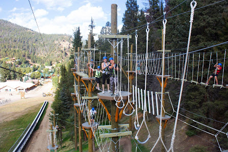 Image of a ski lift ascending through a winter landscape at Red River New Mexico. The scene depicts a ski resort with a challet in the distance part of a bustling winter sports activity.