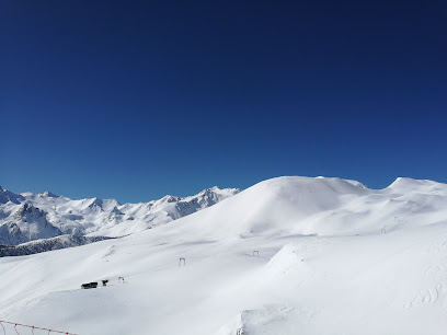 A winter scene at Argentera ski resort, Piedmont, Italy. A chalet nestled near the base of a mountain, with a skier gliding through the snowy landscape.