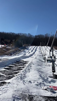 A winter sports scene at Shawnee Mountain Pennsylvania with a ski resort evident. A ski lift can be seen traversing the snow-covered slopes where a skier is also visible.
