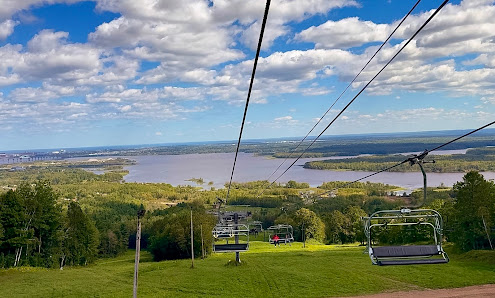 View of Spirit Mountain in Duluth Minnesota with a prominent ski lift ascending the slopes. The image also features a ski resort a challet and a skier enjoying a winter day.