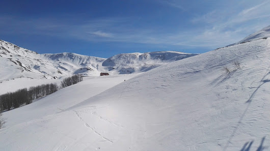 Ski resort in Corno alle Scale, Italy, featuring a charming chalet set against snowy slopes bustling with winter sports activities, including a skier in action.