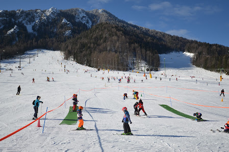 A winter sports scene at Kranjska Gora ski resort in Slovenia, featuring a bustling ski centre and multiple skiers enjoying the snow-covered slopes.