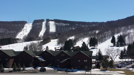 Image of Greek Peak Mountain in New York showing a bustling ski resort. A ski lift ascends the mountain amidst a winter sports scene with snow-covered slopes.