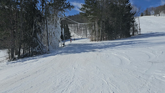 A skier enjoying a run at the Greek Peak Mountain ski resort in Cortland, New York. The winter landscape is filled with pristine snow, a welcoming challet, and a snowmobile parked nearby.