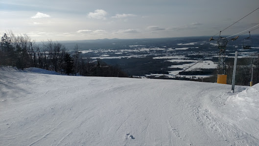 A skier swooshes down the snowy slopes of Bigrock Mountain in Mars Hill Maine with a picturesque chalet and ski resort in the background epitomizing a classic winter sports scene.