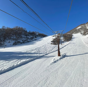 Image showcasing the vibrant scene at Togari Onsen ski resort in Japan, featuring a ski lift ascending a snowy mountain, a skier gliding smoothly down the slope, and a breathtaking winter backdrop.