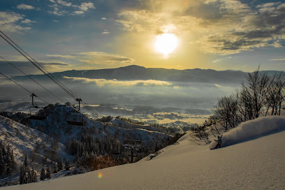 Winter sports scene at Togari Onsen in Nagano, Japan, featuring a bustling ski resort against a stunning backdrop of snow-covered mountainous terrain and a functional ski lift.