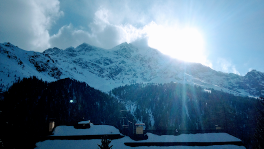 A charming challet at the Skilifte und Sesselbahn Sarn Heinzenberg in Eastern Switzerland, nestled amidst a breathtaking winter scenery. A sunny day illuminates the scenic view of the mountain and the bustle of winter sports activities.