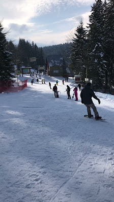 Winter scene at Clăbucet ski resort in Predeal, Brașov, Romania featuring a skier and a family enjoying skiing amidst picturesque settings, with a charming challet in the backdrop.