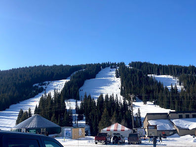 A view of Antelope Butte ski resort in Shell Wyoming featuring a ski lift travelling over the snow-covered slopes against the backdrop of a majestic mountain.