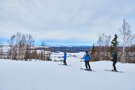 Winter scene at Mont Lac-Vert, Quebec with smiling skier gliding down a snowy slope. The ski resort and a group of skiers can be seen in the backdrop, enjoying winter sports activities.