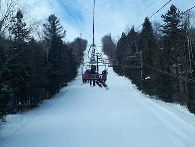 Ski lift ascending at Belle Neige Ski Resort in Laurentides, Quebec, with skiers enjoying winter sports. The chalet nestled in the snowy landscape adds a cozy charm to the scene.