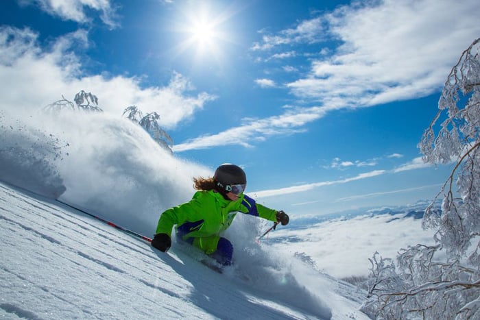 A skier and snowboarder navigate a winter sports scene at Niseko United ski resort in Hokkaido, Japan. A child can be seen tentatively learning to ski amidst the snow-capped landscape.