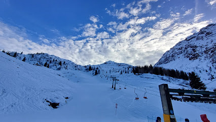 Image of Nuova Lizzola in Lombardy, showcasing a charming chalet, a lively winter sports scene at a ski resort, complete with a visible ski lift highlighted against the backdrop of an imposing mountain.