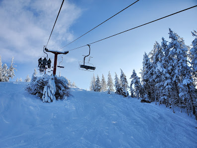 A ski lift ascends Harper Mountain at a ski resort in Kamloops British Columbia. Skiers enjoy the winter sports scene around a quaint chalet.
