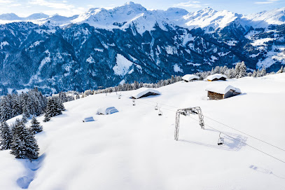 A delightful winter sports scene at Sportbahnen Hochwang in Eastern Switzerland. A charming mountain hut stands against a backdrop of snowy slopes bustling with skiers at the resort.