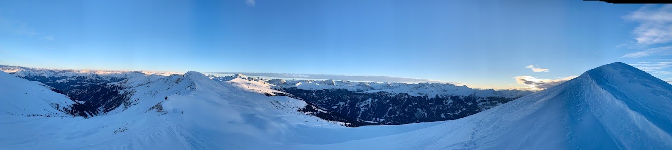 Sunny scene at Sportbahnen Hochwang ski resort in Switzerland, including a chalet, winter sports activity on the mountain, and clear blue skies.