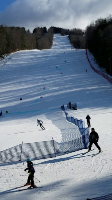 A skier enjoying a winter day at Berkshire East in Charlemont, Massachusetts. The scene depicts a bustling ski resort with a cosy chalet and a well-equipped winter sports centre in the backdrop.