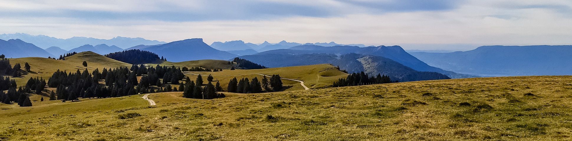 Station du Semnoz in France - a grassy hill with trees and mountains in the background.