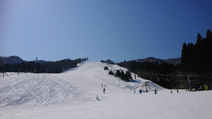 Winter scene at Okukan ski resort in Toyooka, Japan. Visible are skiers enjoying the slopes, a ski lift in operation and a charming chalet nestled in the snow-blanketed landscape.