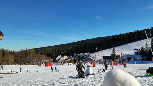 Winter sports scene at Chalmazel in France, featuring a sports centre and a chalet amidst a ski resort. A lone skier among snowy slopes enhances the Alpine landscape.