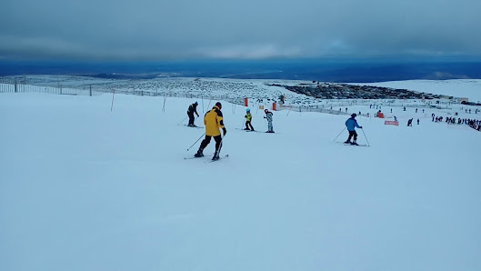 Winter sports scene at Ski Sierra Bejar Covatilla in Salamanca, Spain, featuring a bustling winter sports centre and multiple skiers, including a family, dotting the snowy slopes.