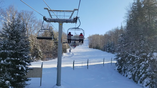 Winter scene at Sommet Olympia in Quebec, Canada, featuring a ski lift ascending the snowy mountain. Skiers and snowmobiles are faintly visible against the snowy backdrop, adding to the ambience of the ski resort.