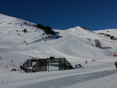 View of Val Louron in France featuring a chalet and a ski resort amidst a winter sports scene. The pristine snow-covered slopes are visible in the background.