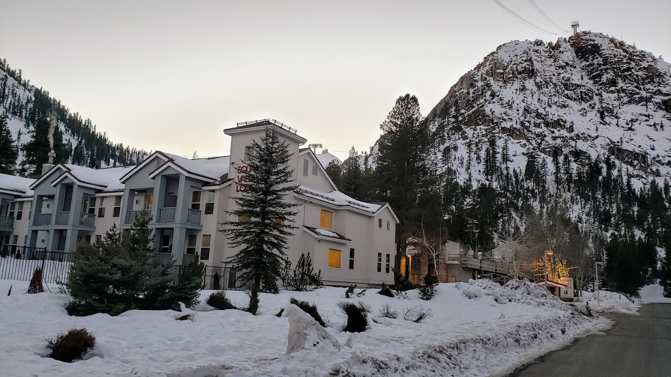 Winter scene at Palisades Tahoe in Lake Tahoe, California, showcasing clear skies, snowy mountains and a bustling ski resort teeming with winter sports enthusiasts.