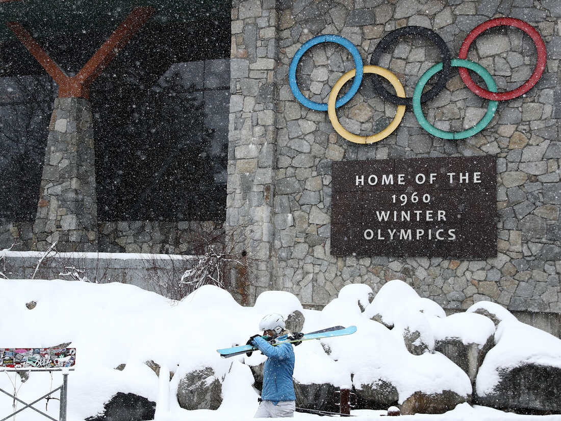 Palisades Tahoe in USA: a man holding a snowboard in front of a stone building.