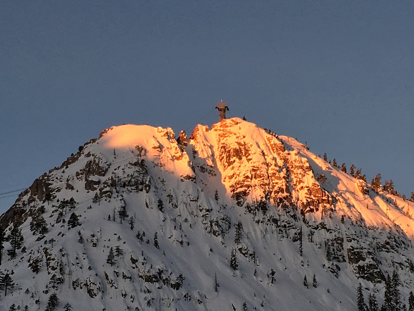 View of Palisades Tahoe in Lake Tahoe, California, showcasing a majestic mountain covered in snow, with a cozy chalet nestled at the base, and activity of a bustling ski resort.